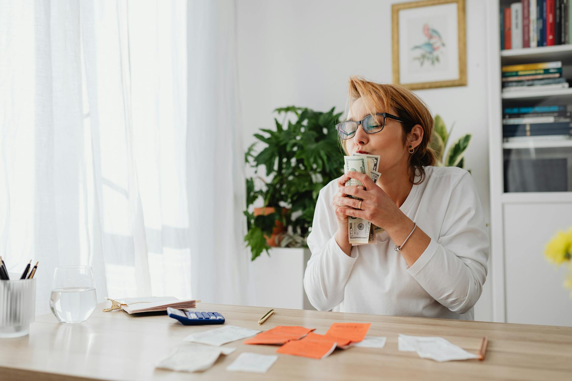 Smiling woman holding banknotes at a desk, celebrating financial success and freedom.