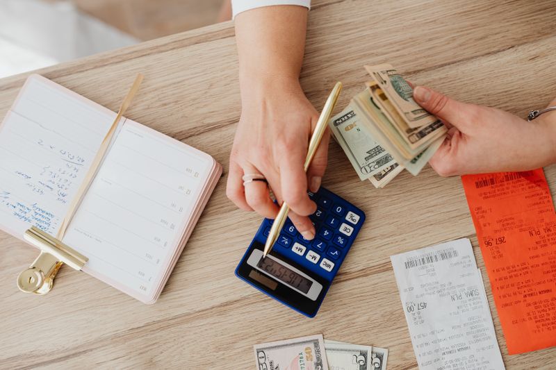 Hands managing finances with calculator, cash, and receipts on a wooden table. Ideal for budgeting concepts.