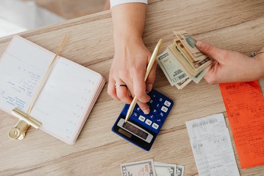 Hands managing finances with calculator, cash, and receipts on a wooden table. Ideal for budgeting concepts.