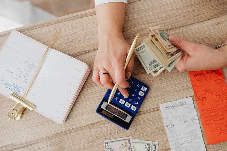 Person Holding Paper Bills While Using A Calculator