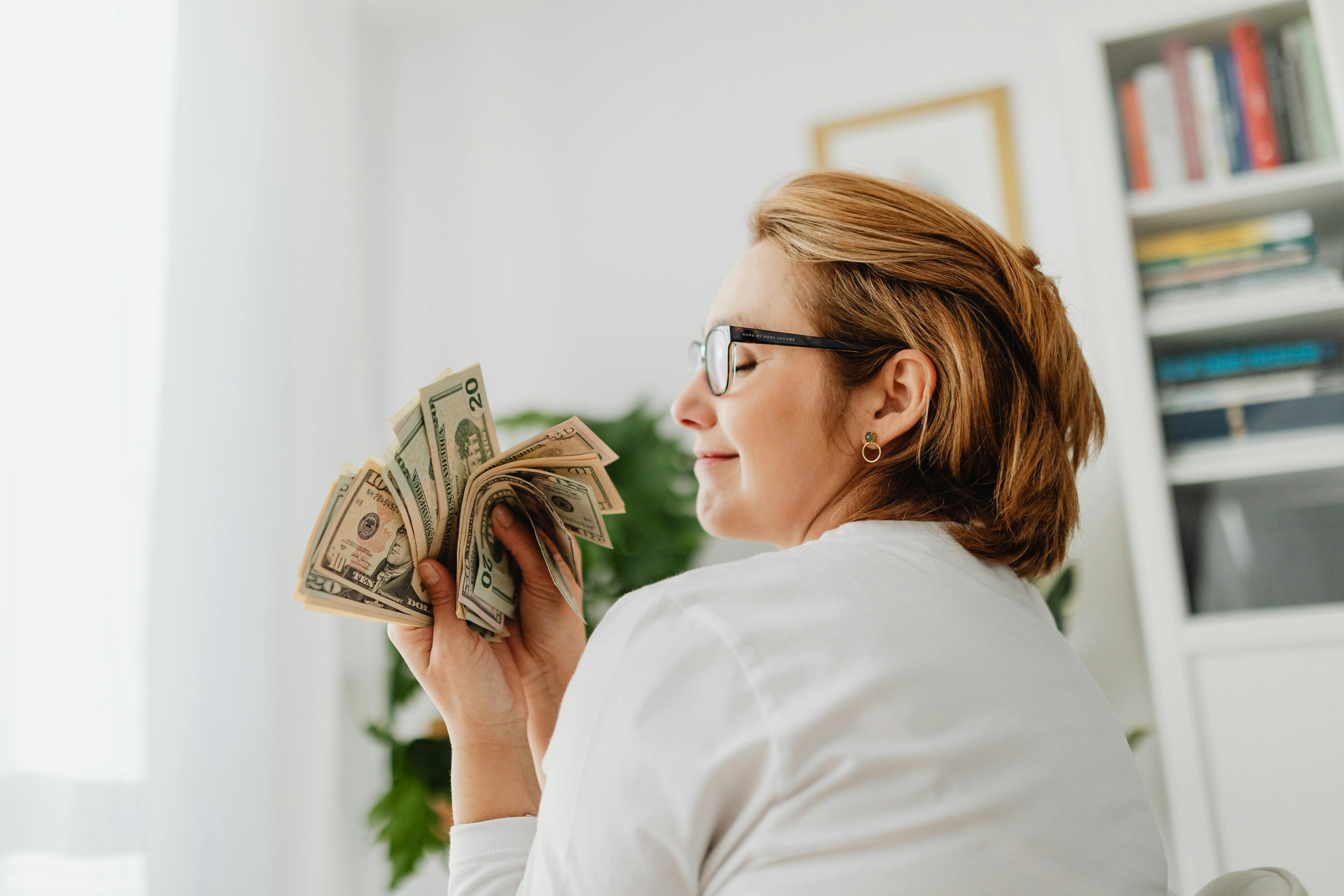 Free Confident woman in glasses holding US dollar bills, symbolizing wealth and finance. Stock Photo