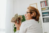 一位戴眼镜的自信女性手持美钞，象征着财富与金融
