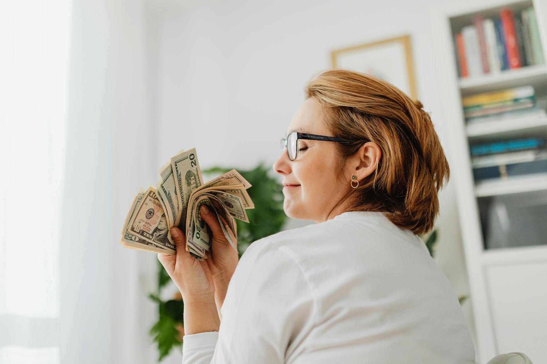 Confident woman in glasses holding US dollar bills, symbolizing wealth and finance.