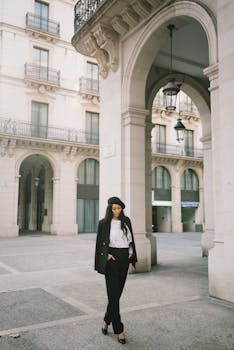 Fashionable woman in a stylish black and white ensemble walking confidently beneath urban arches.