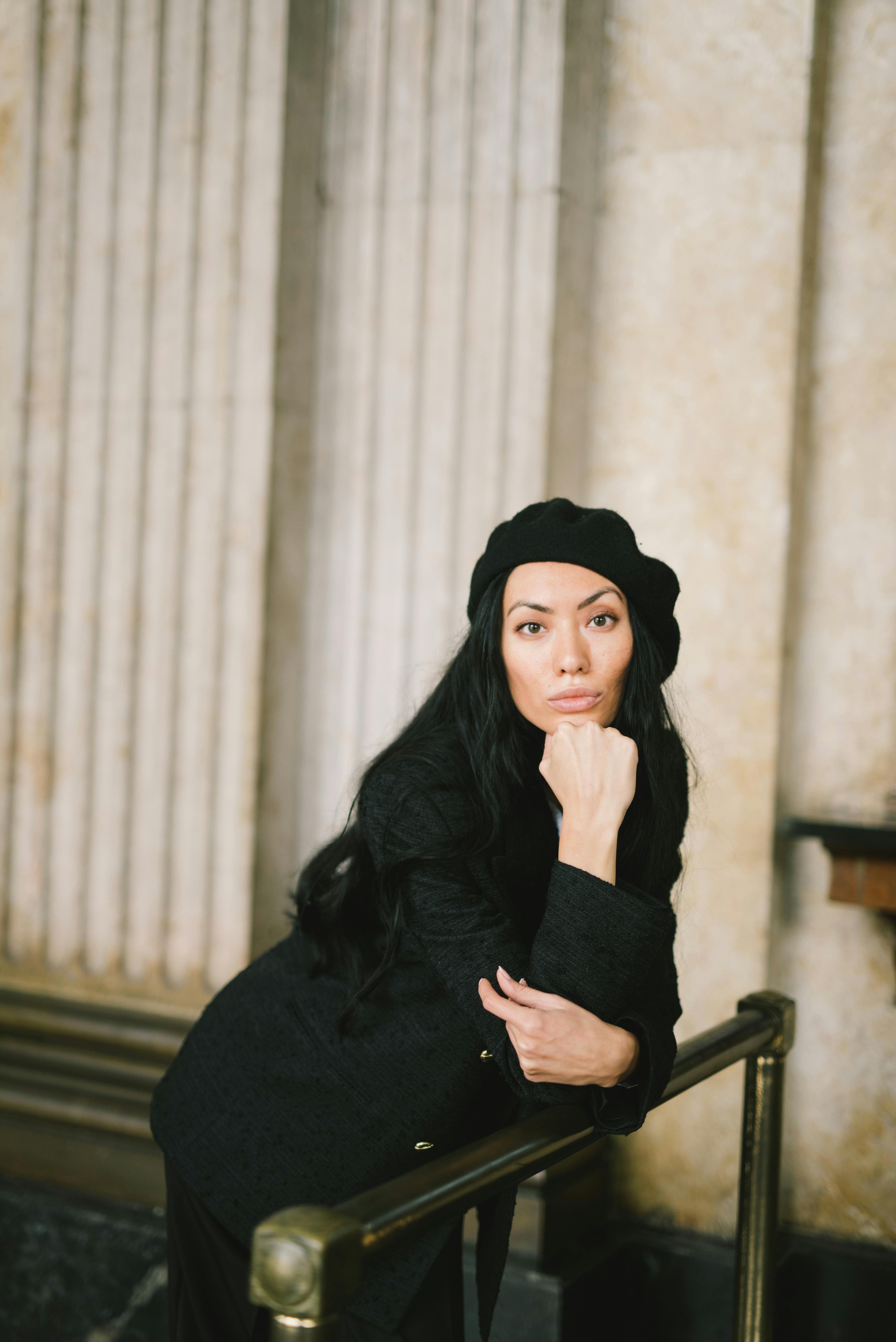 woman in black coat and black beret hat posing with her hand under chin