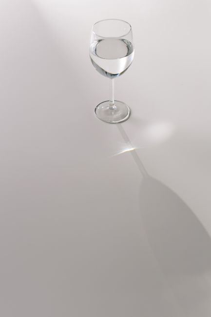 A minimalist shot of a wine glass filled with water casting a subtle shadow on a white background.