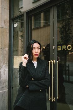 一位身着时尚黑色外套的精致女子，正站在玻璃门旁，散发着自信与时尚的气息