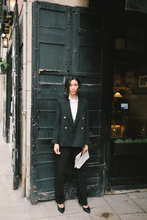 бесплатная Женщина в черном пальто стоит у черной деревянной двери Стоковое фото