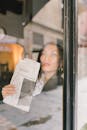 Woman near the Glass Wall Holding a Newspaper