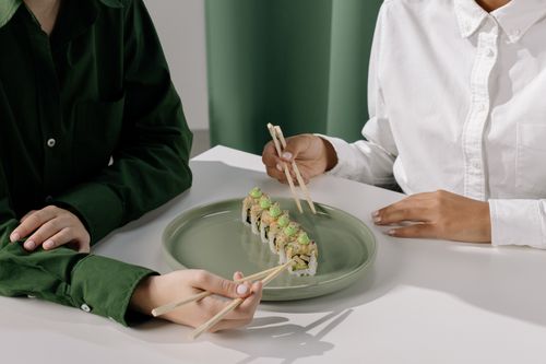 Free Two people enjoy sushi with chopsticks on a stylish plate indoors, showcasing traditional Asian dining. Stock Photo