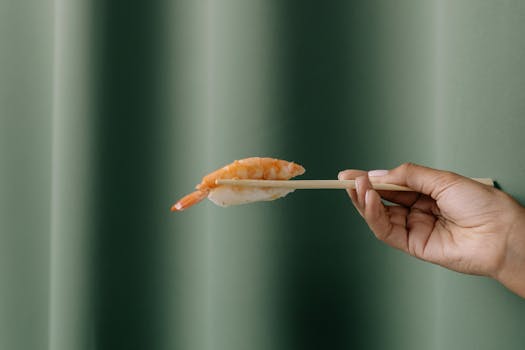A hand holding sushi with chopsticks against a green background. Elegant and minimal capture of Japanese cuisine.