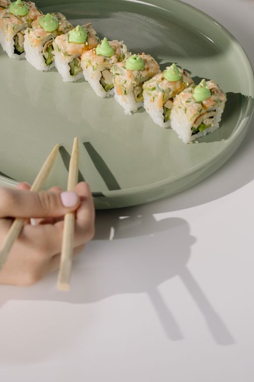 Free Sushi rolls topped with wasabi on a ceramic plate, with chopsticks visible. Stock Photo