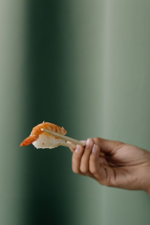 Free A hand holding shrimp nigiri sushi with chopsticks against a blurred green background. Stock Photo