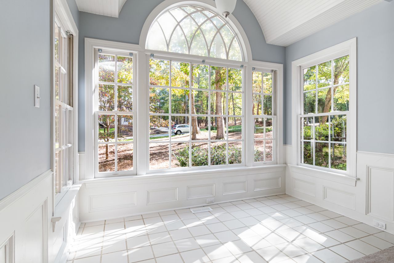Empty bright sunroom with arched windows and white tile flooring