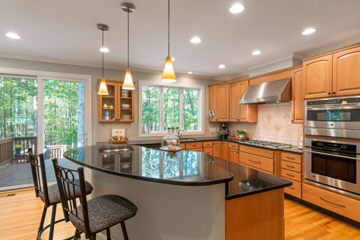 Bright modern kitchen with granite island, wooden cabinets, and stainless steel appliances.