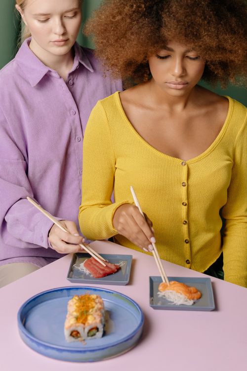 Free Two women enjoying a variety of sushi dishes with chopsticks indoors, capturing the essence of Japanese cuisine. Stock Photo