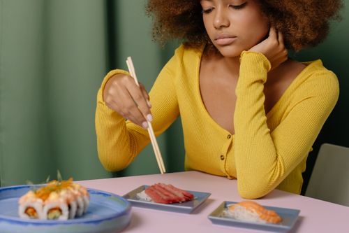Free A woman in a yellow top eating sushi with chopsticks, featuring nigiri and sashimi. Stock Photo