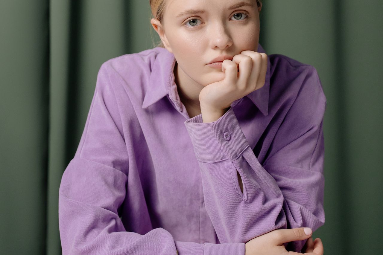 portrait of a young woman in a purple shirt with hand on chin looking
