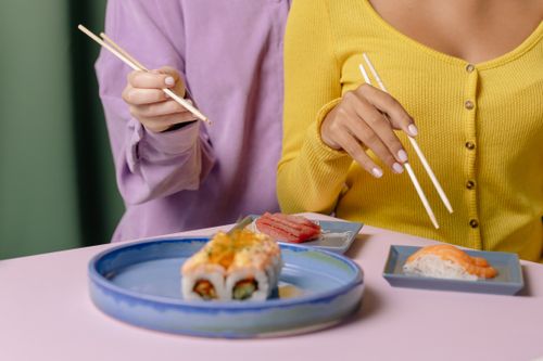 Free Two people enjoying a sushi meal with chopsticks, vibrant clothing adds color. Stock Photo