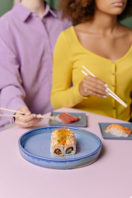 Free A vibrant close-up of sushi rolls with people dining in the background, emphasizing food enjoyment. Stock Photo