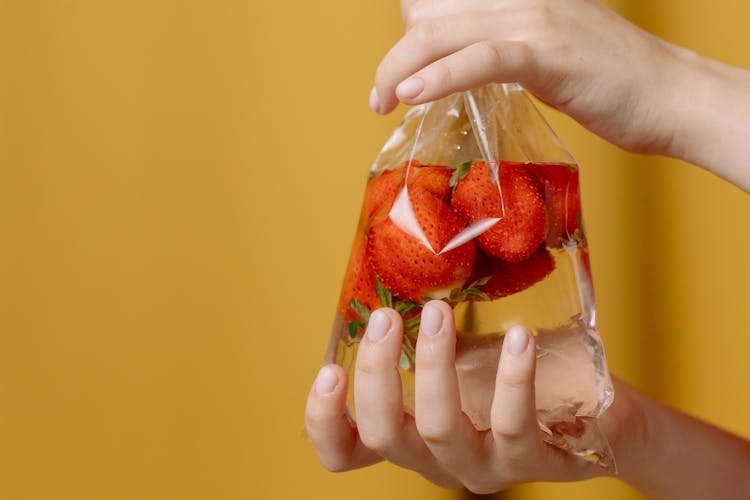 Hands Holding Plastic Bag With Water And Strawberries