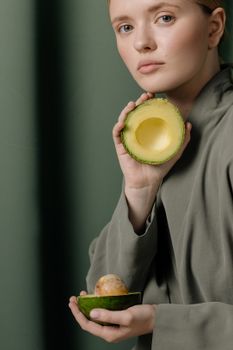 一位身穿绿色服装的女士表情严肃，在绿色背景下拿着切成薄片的鳄梨