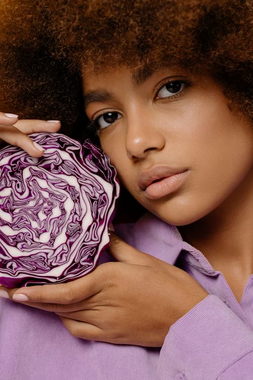 Free Close-up portrait of a woman with afro hair holding half a red cabbage, symbolizing freshness and vegan lifestyle. Stock Photo