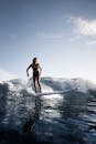 Cheerful female surfer in swimwear standing on surfboard on sea on summer day