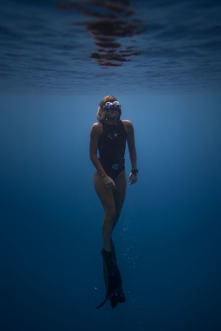Full body of unrecognizable sportswoman floating underwater in black swimsuit with snorkeling mask and flippers in deep sea