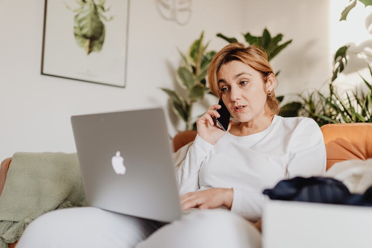 Woman Sitting On A Couch Using Laptop And Talking Through the Phone 