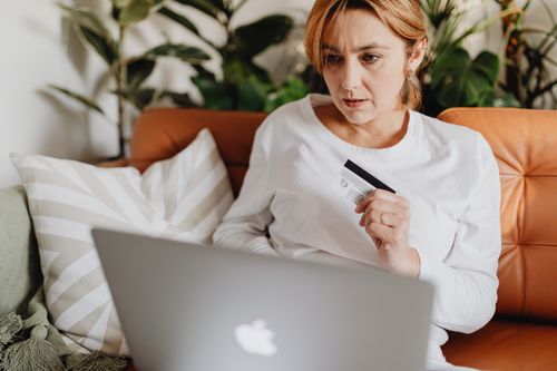 Free A woman sitting on a couch shopping online with a credit card and laptop in a cozy living room. Stock Photo