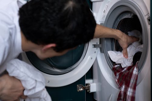 Free Close-up of a man placing clothes into a washing machine during household chores. Stock Photo