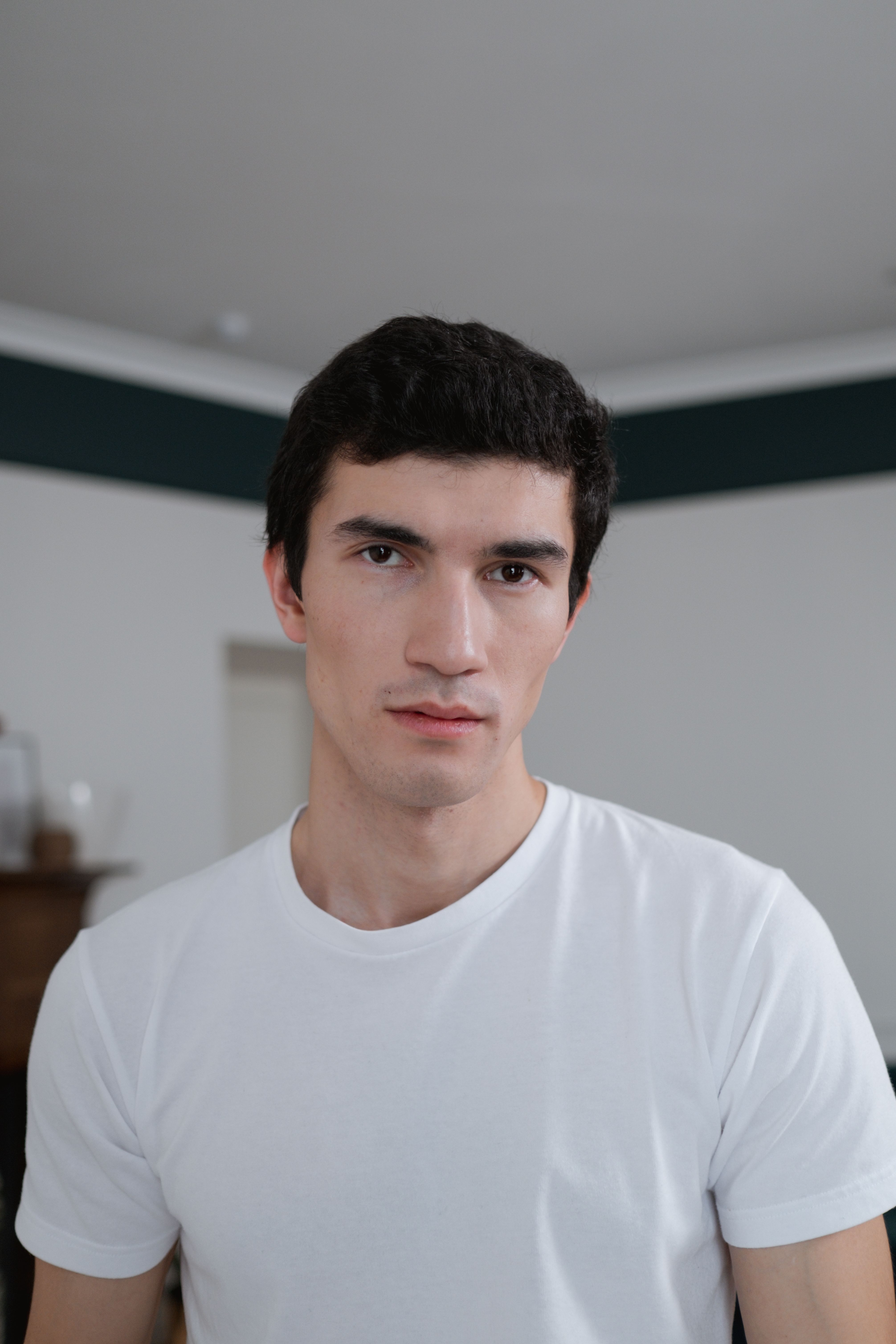 A focused portrait of a man indoors wearing a white shirt.