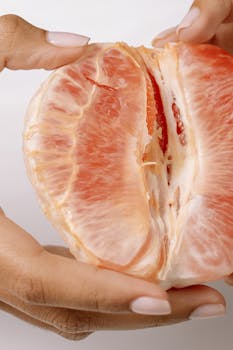Detailed image of hands peeling a ripe grapefruit, showcasing juicy pink flesh.