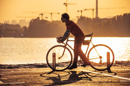 Free Silhouette of a cyclist biking by the river during a stunning sunset view. Stock Photo