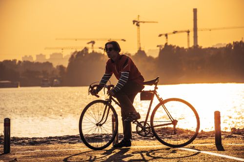 Free Man biking along a waterfront path at sunset, highlighting outdoor activity and tranquility. Stock Photo