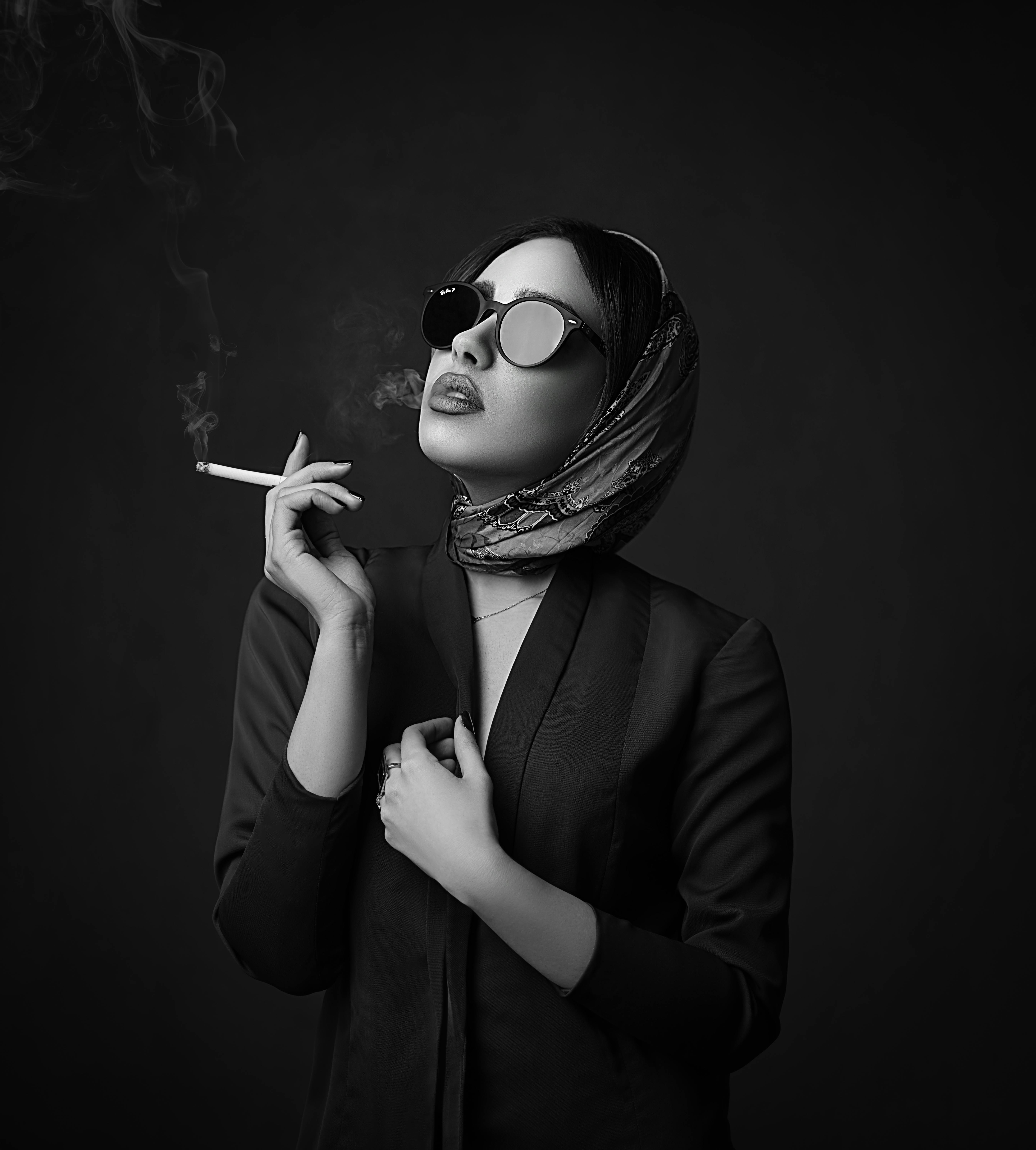 在单色背景下，一位优雅的女人戴着太阳镜和头巾吸烟