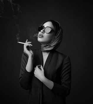 在单色背景下，一位优雅的女人戴着太阳镜和头巾吸烟