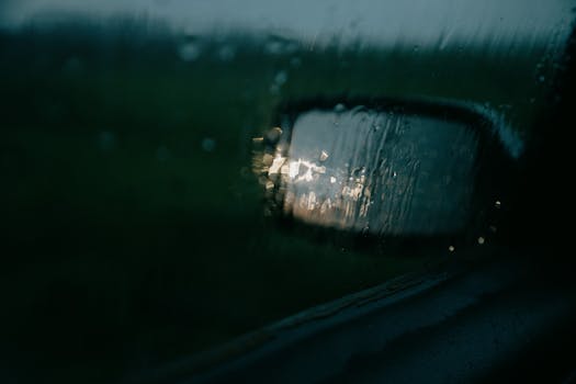 Raindrops on car window reflecting light in a gloomy countryside drive.