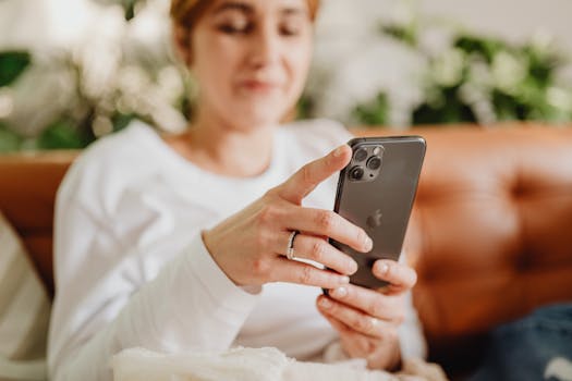 Woman attentively browsing smartphone while relaxing on a comfortable couch indoors.