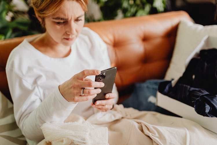 Woman Sitting On A Couch And Scrolling Through Her Phone 