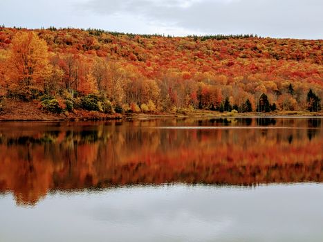 Tranquil autumn landscape with vibrant foliage reflecting in a mountain lake in West Virginia.