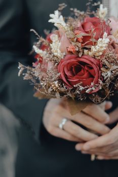 Close-up of a bridegroom holding a beautiful bouquet with red roses and dried flowers.