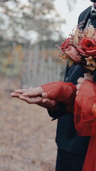 A close-up of a couple holding hands and flowers in an autumn outdoor setting.