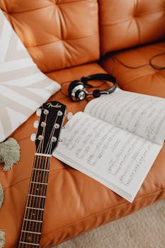 An acoustic guitar, headphones, and sheet music rest on a cozy leather sofa.