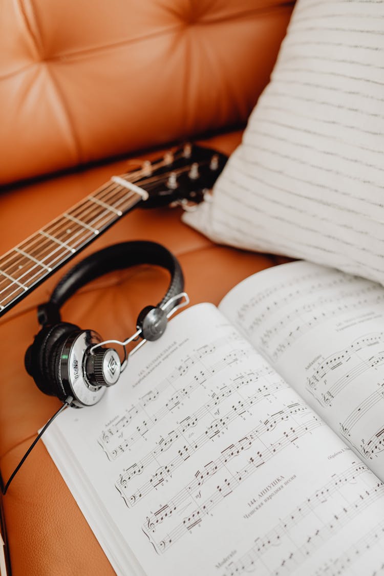 Guitar, Headphones And A Music Sheet On A Couch 