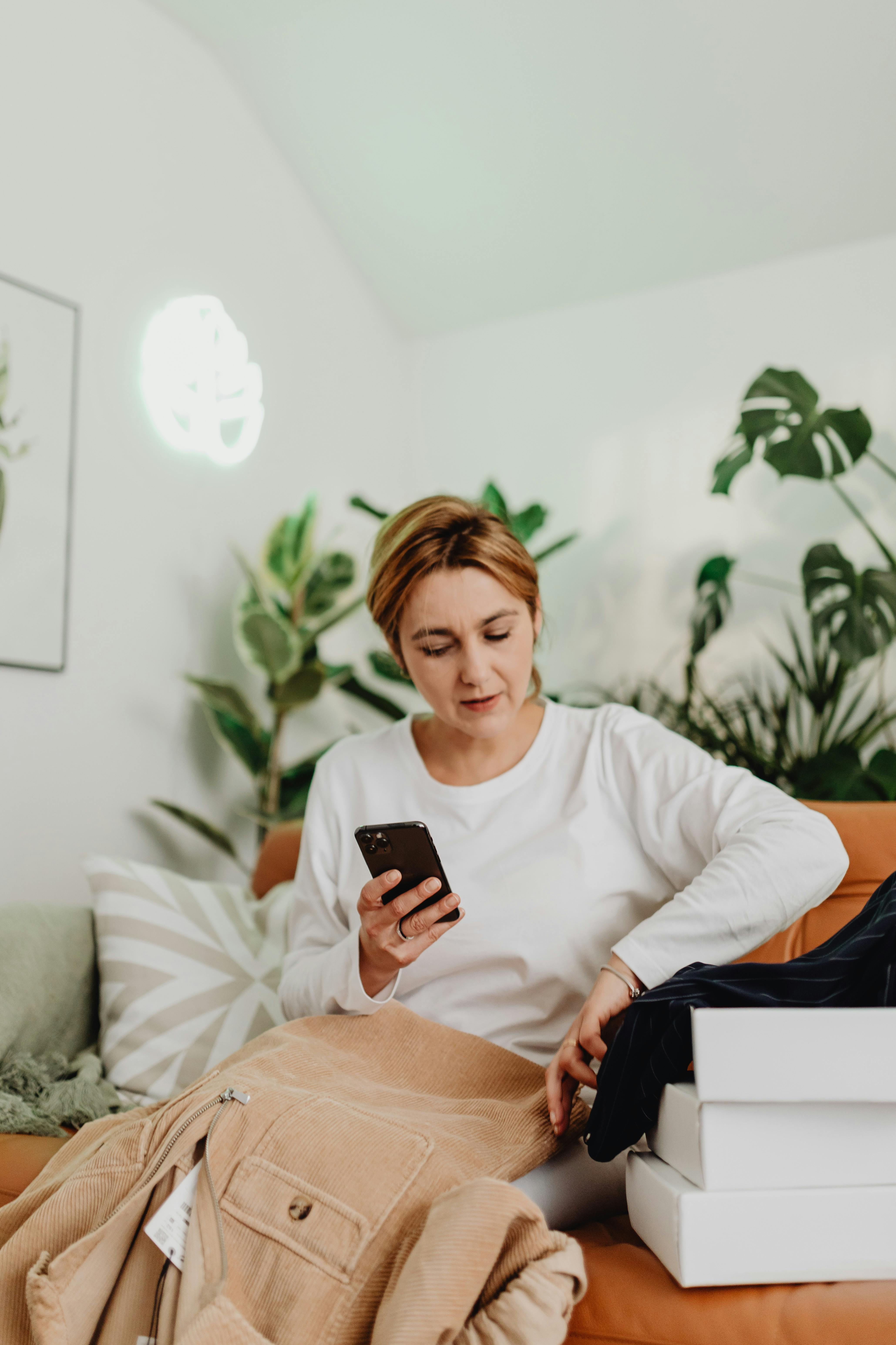 woman sitting on sofa and opening boxes with clothes shopping