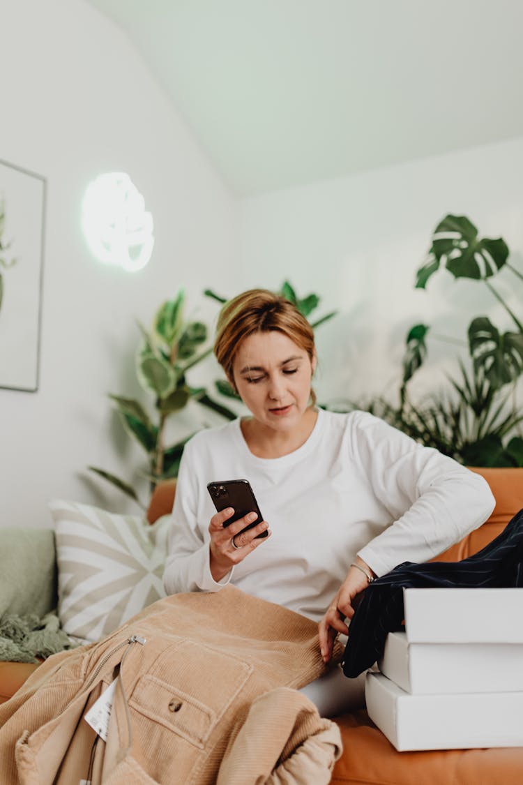 Woman Sitting On Sofa And Opening Boxes With Clothes Shopping