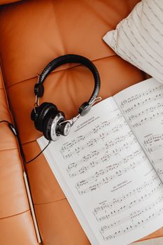 Black headphones resting on music sheets over a tan leather sofa.