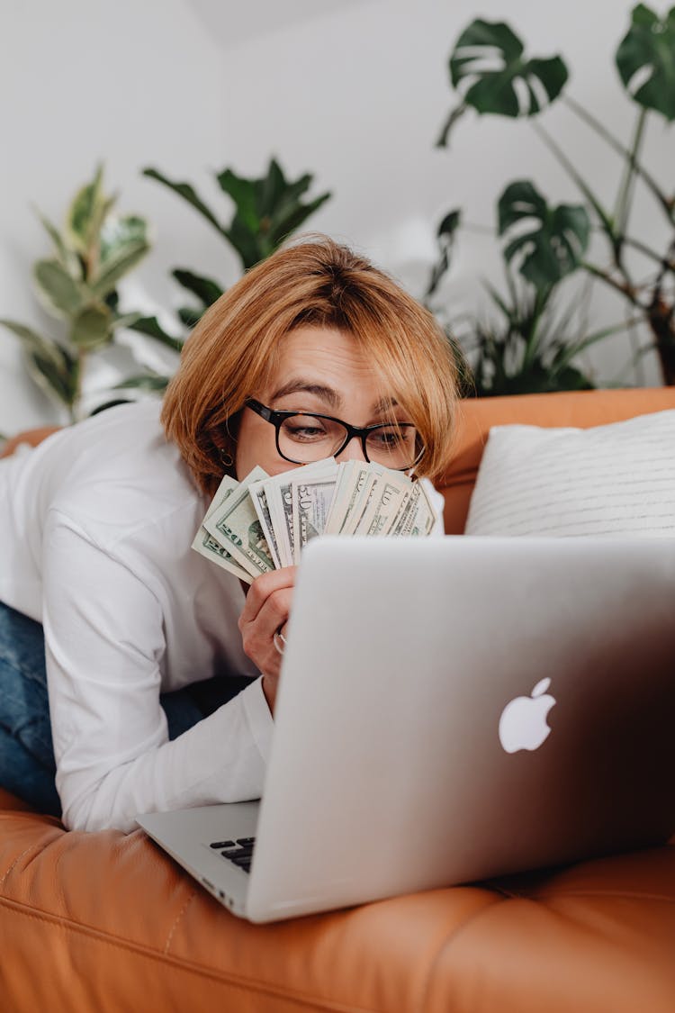 Woman Sitting In Front Of A Laptop And Covering Half Of Her Face With Cash 